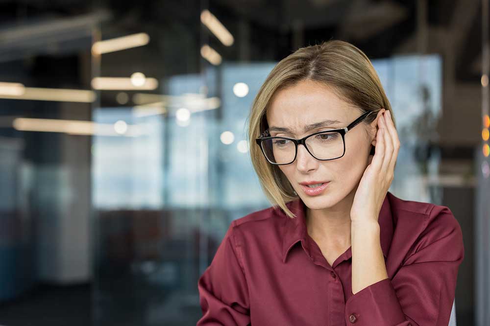 Worried woman in glasses touching her ear, as when hearing aids sound uneven, from West Valley Hearing Center in Woodland Hills, CA